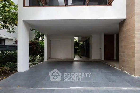 Modern residential building entrance with spacious parking area and lush greenery.