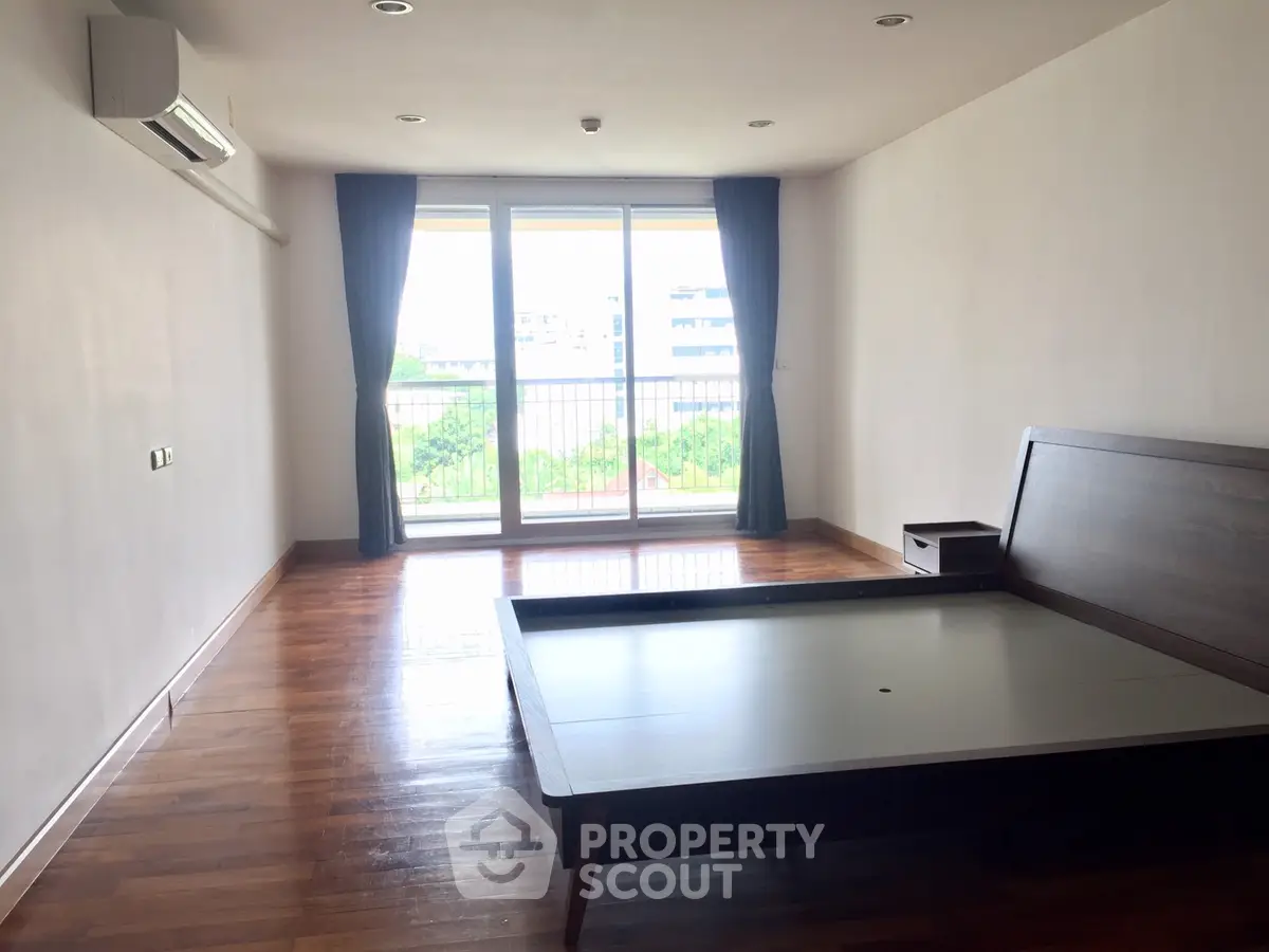 Spacious bedroom with wooden flooring and large window offering natural light.