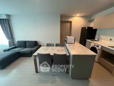 Modern open-layout living room with kitchen, featuring sleek furniture and appliances.
