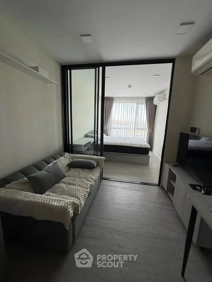 Modern apartment with cozy living room and bedroom separated by glass sliding doors.