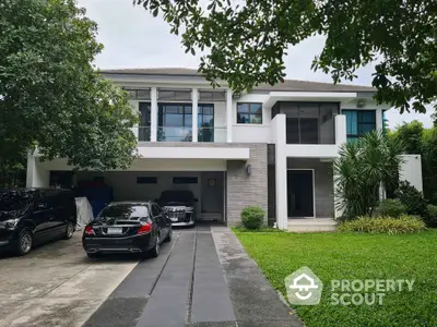 Modern two-story house with sleek design and lush green lawn, featuring a spacious driveway and luxury cars.