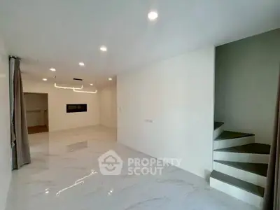 Spacious modern living room with elegant staircase and sleek lighting, perfect for contemporary living.