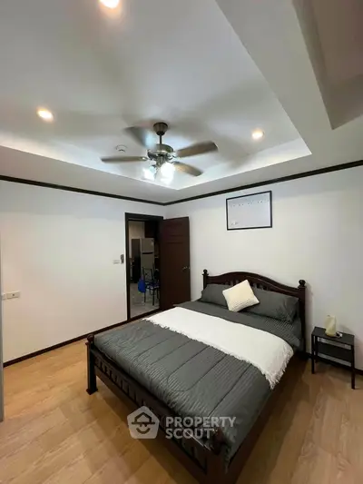 Spacious bedroom with elegant wooden bed and ceiling fan in modern apartment.