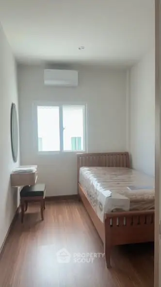 Cozy bedroom with wooden flooring and natural light, featuring a comfortable bed and a wall-mounted mirror.