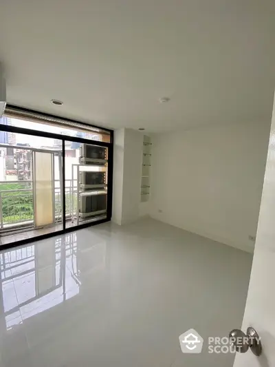 Spacious minimalist room with large windows and balcony access in modern apartment.