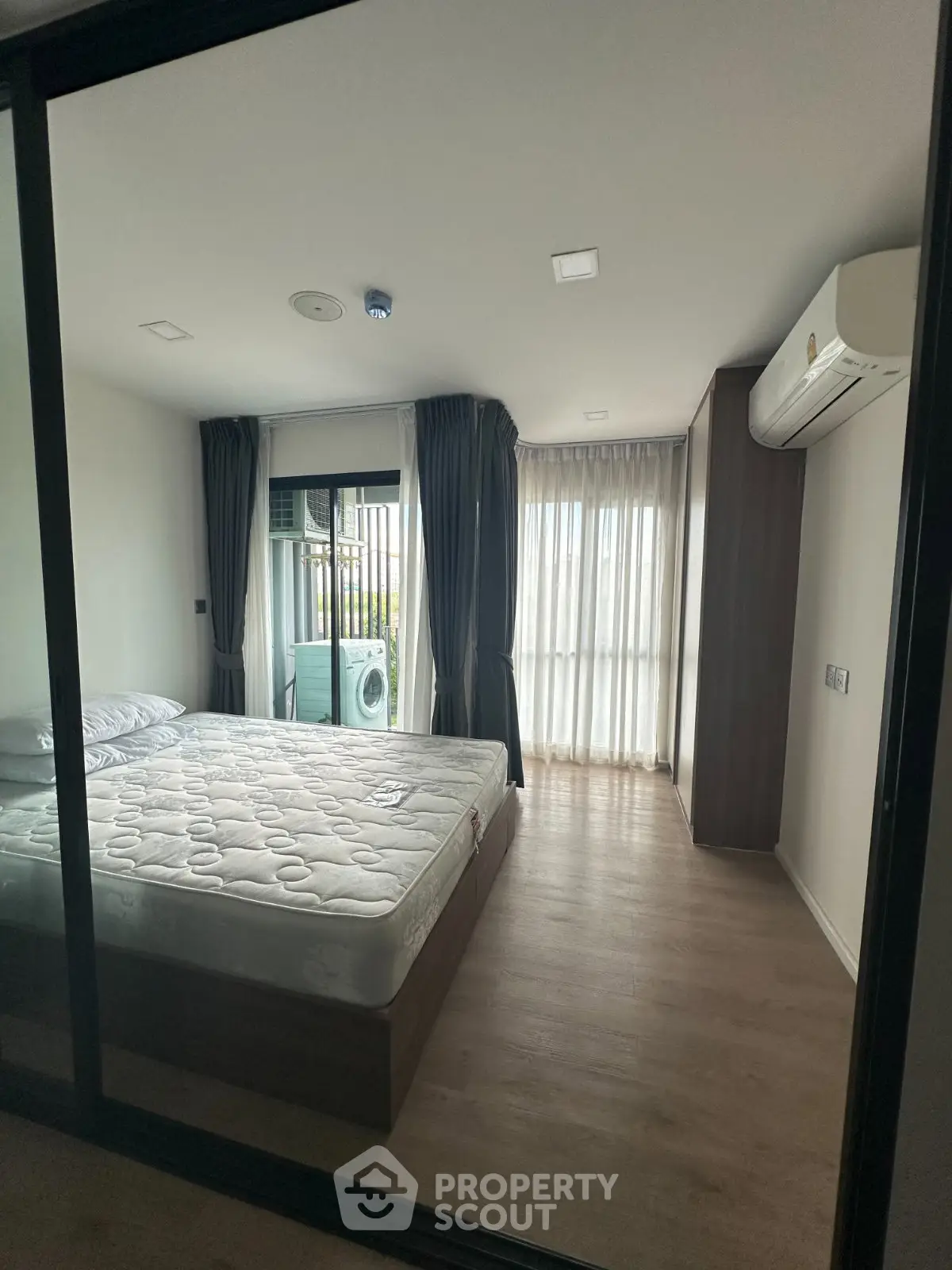 Modern bedroom with large window, air conditioning, and washing machine in a sleek apartment.