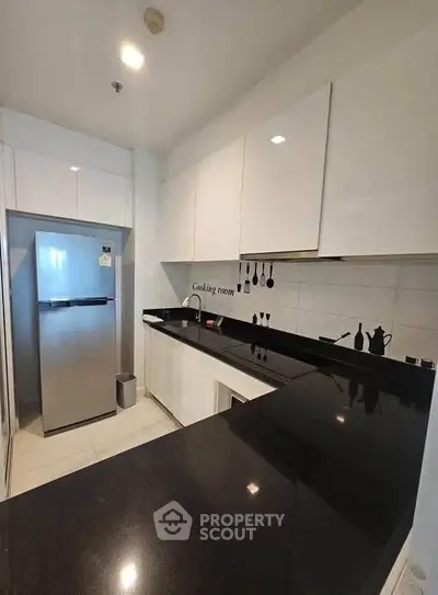 Modern kitchen with sleek black countertops and stainless steel fridge in a compact layout.