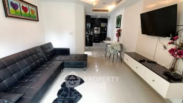 Modern living room with sleek black sofa and wall-mounted TV, leading to a stylish kitchen.