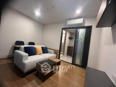 Modern living room with sleek furniture and wooden flooring, featuring a cozy sofa and air conditioning.