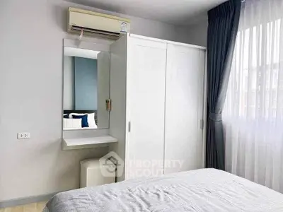 Bright bedroom with modern white wardrobe and air conditioning, featuring a cozy bed and natural light from large window.
