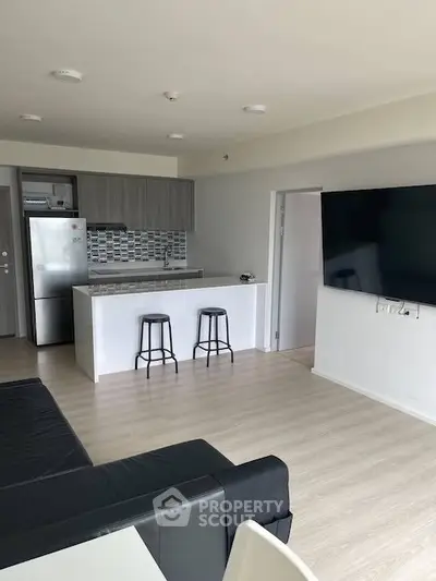 Modern open-plan living room with sleek kitchen and large wall-mounted TV