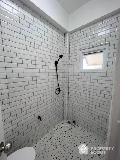 Sleek modern bathroom with white subway tiles and contrasting black fixtures, featuring a walk-in shower with stylish terrazzo flooring and natural light from a small window.