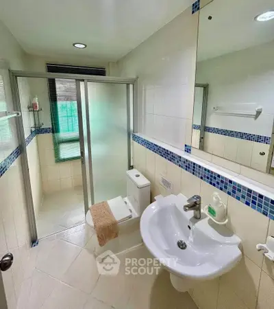 Modern bathroom with glass shower and stylish sink in a bright, tiled space.