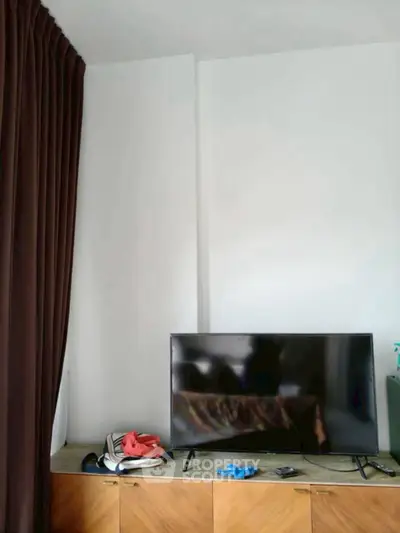 Modern living room with sleek TV and stylish wooden cabinet, complemented by elegant dark curtains.