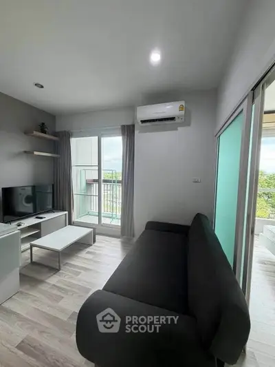 Modern living room with sleek black sofa, TV, and balcony view in a stylish apartment.