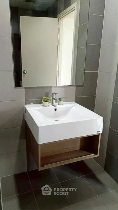 Modern bathroom with sleek sink and mirror, featuring stylish gray tiles and minimalist decor.