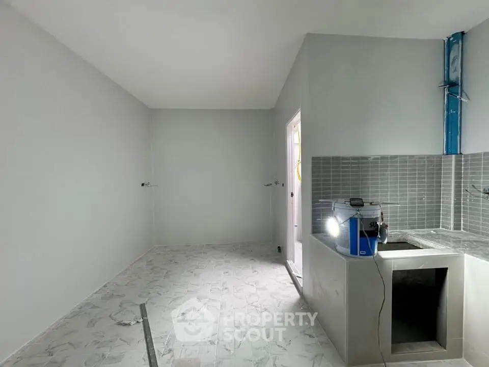 Spacious kitchen under renovation with modern tile flooring and sleek gray backsplash.