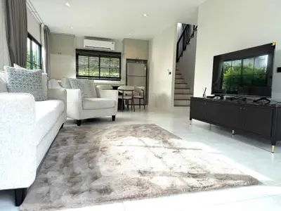 Spacious modern living room with plush rug and stylish furniture, open layout leading to kitchen and staircase.