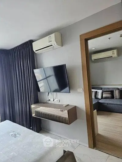 Modern bedroom with wall-mounted TV and air conditioning, adjacent to a cozy living room.