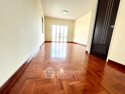 Spacious empty room with polished wooden floors and large window for natural light.