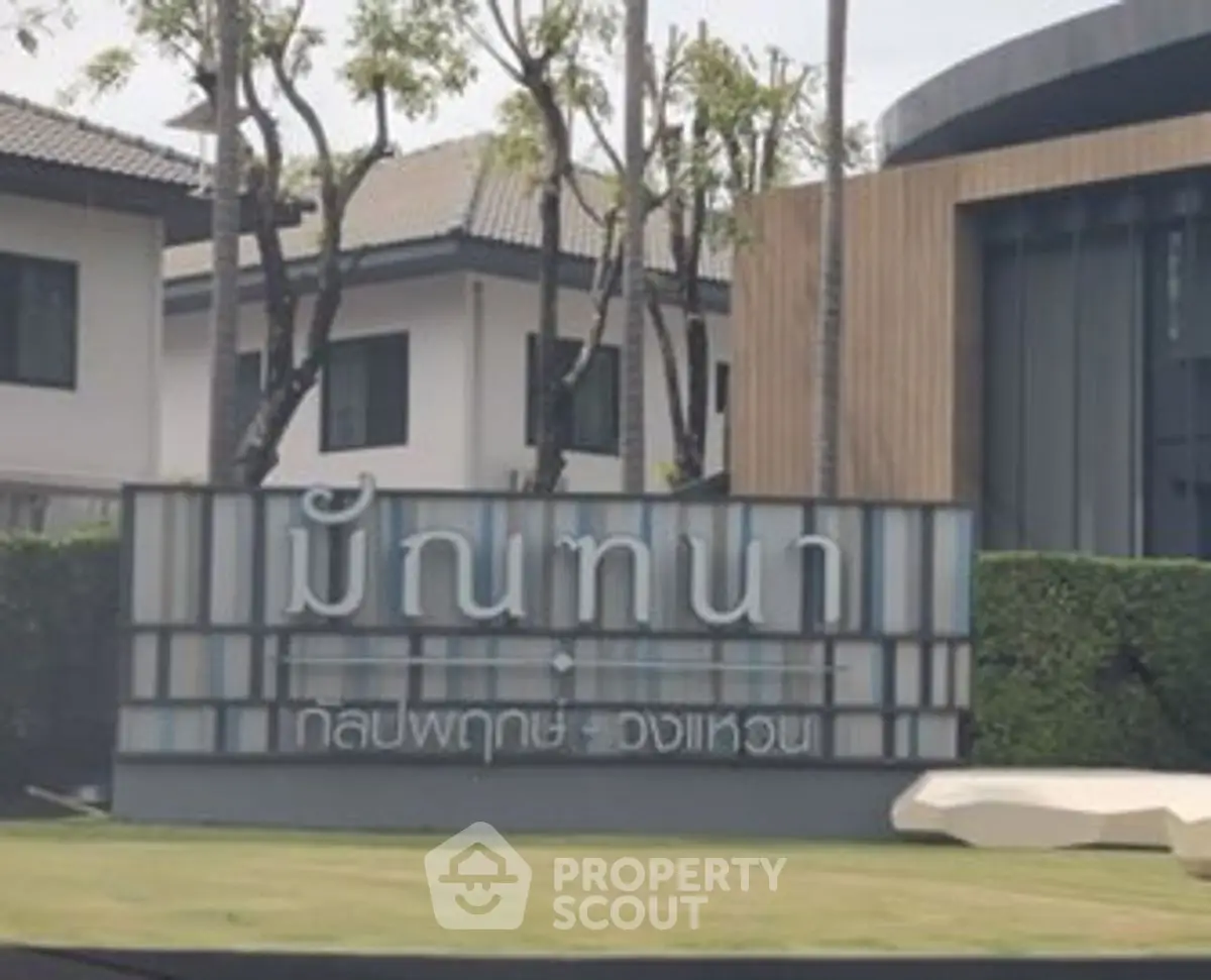 Modern residential building entrance with stylish signage and lush greenery.