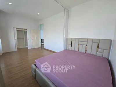 Spacious bedroom with modern design and ample natural light, featuring a stylish bed and wooden flooring.