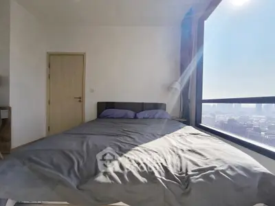 Bright bedroom with large window offering stunning city view, modern furnishings, and ample natural light.