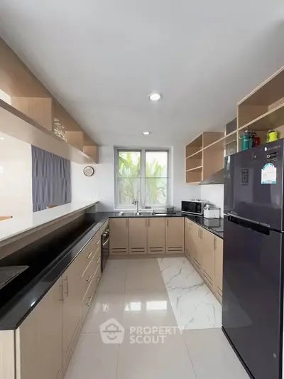 Modern kitchen with sleek cabinetry, black countertops, and large window for natural light.
