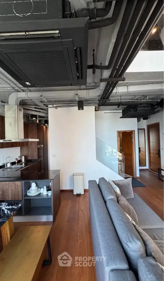 Modern industrial-style living room with open kitchen and sleek furnishings.
