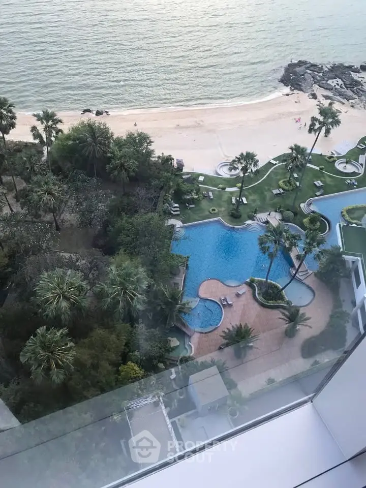 Stunning beachfront view with luxurious pool and lush greenery from high-rise apartment.