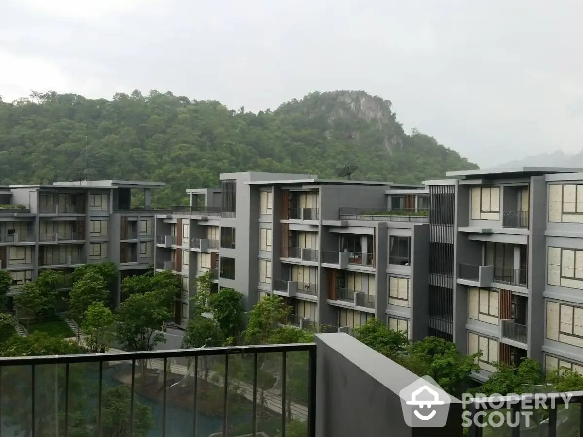 Serene mountain view from a modern apartment complex balcony, showcasing lush greenery and contemporary architecture in a tranquil setting.