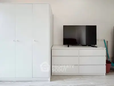 Modern minimalist bedroom with sleek white wardrobe and TV on dresser