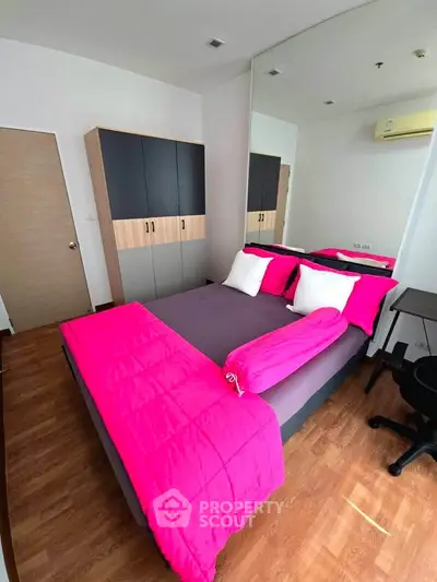 Modern bedroom with vibrant pink bedding and mirrored wardrobe, featuring sleek wooden flooring and minimalist decor.