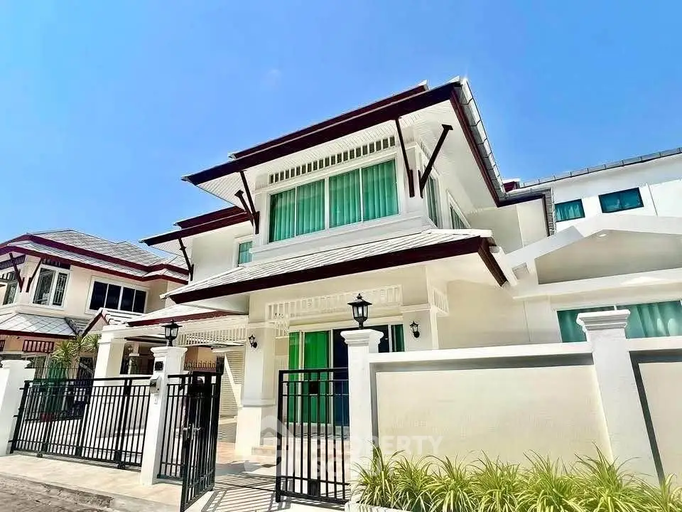 Stunning modern two-story house with elegant design and gated entrance under a clear blue sky.