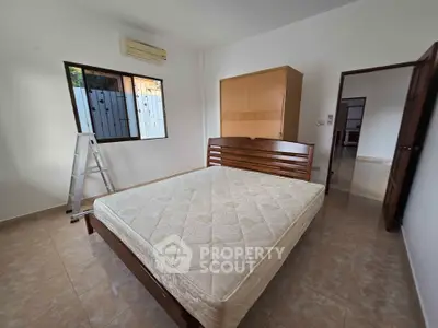 Spacious bedroom with wooden bed frame and wardrobe, featuring tiled flooring and air conditioning.