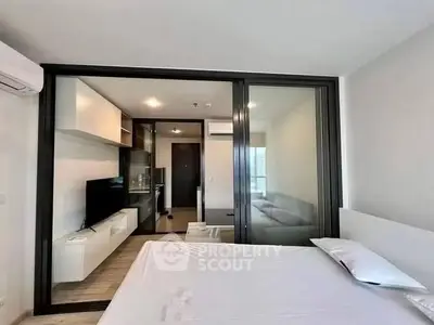 Modern bedroom with sliding glass doors leading to a stylish living area, featuring sleek furniture and ample natural light.