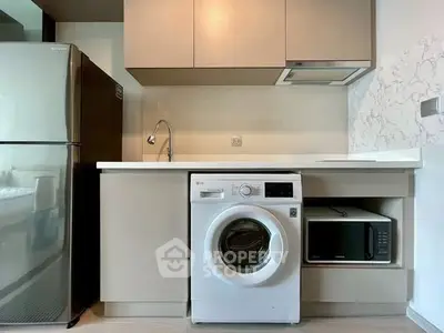 Modern kitchen with washing machine, fridge, and microwave in sleek cabinetry.