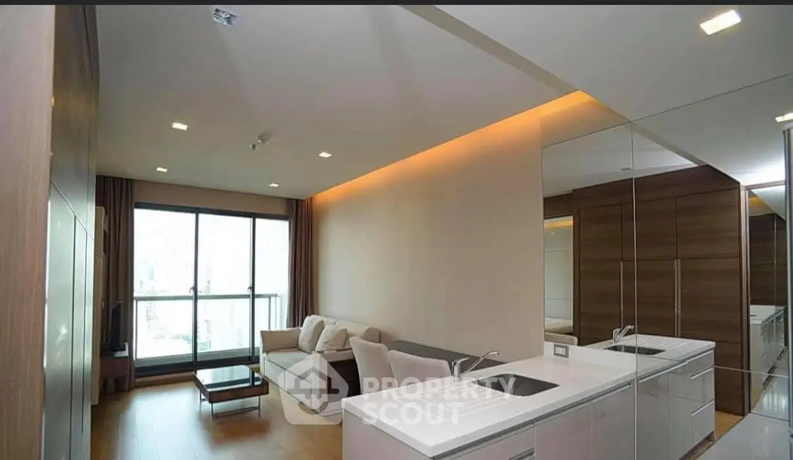 Modern living room with open kitchen and large windows offering city views.