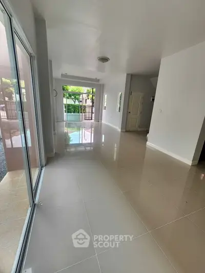 Spacious open-plan living area with glossy tiled floors and large windows offering garden views.