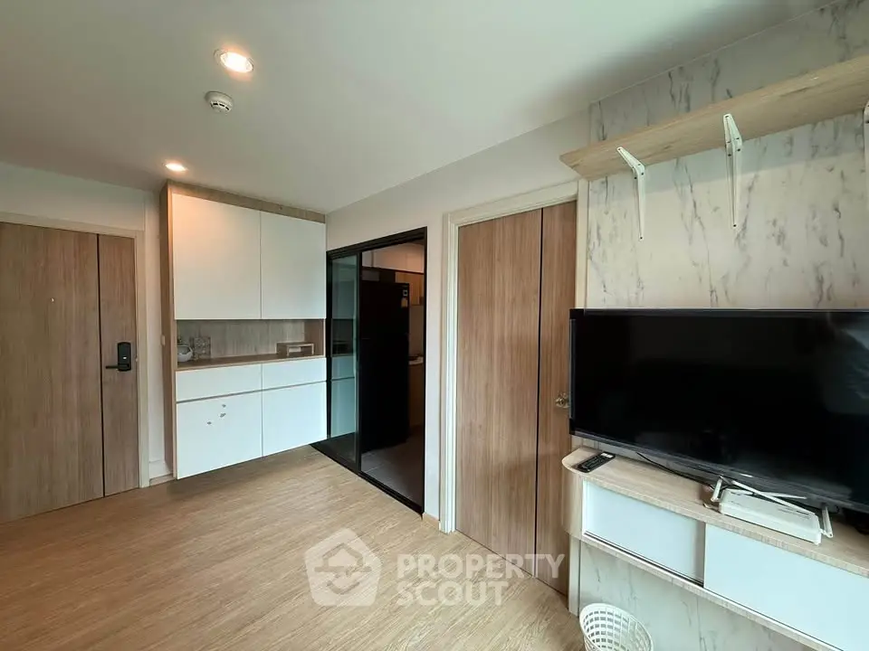 Modern living room with sleek wooden flooring and built-in storage, featuring a flat-screen TV and stylish decor.