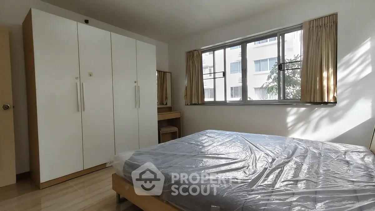 Spacious bedroom with large window and modern wardrobe in a bright apartment.