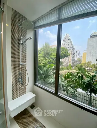 Modern bathroom with large window offering stunning city view and lush greenery.