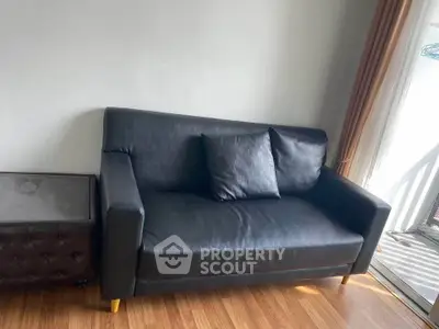 Modern living room with sleek black leather sofa and natural light.