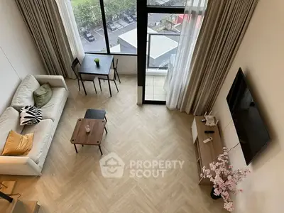 Modern living room with high ceiling and large windows offering natural light and city view.