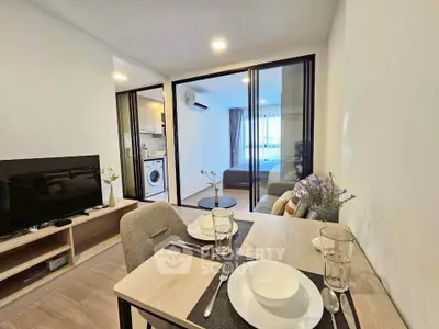 Modern open-plan living room with dining area and view into bedroom, featuring sleek furniture and natural light.