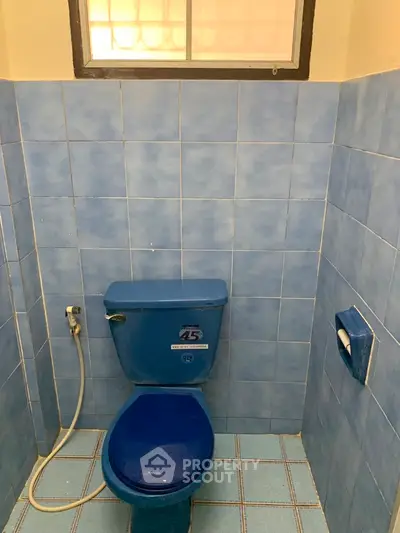 Compact blue-tiled bathroom with window and toilet, ideal for small spaces.