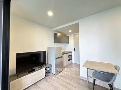 Modern compact living room with kitchen, featuring sleek furniture and bright lighting.