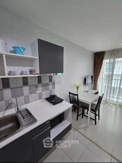 Modern kitchen with dining area, featuring sleek cabinetry and natural light from large windows.