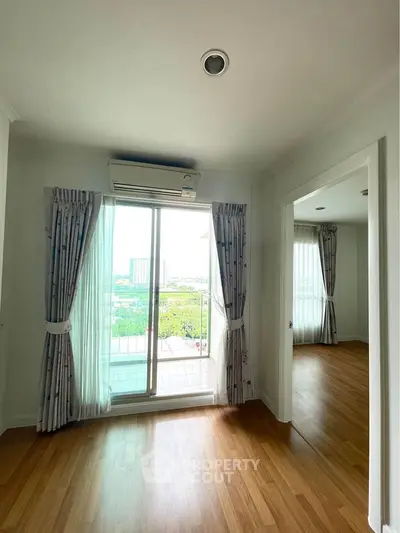 Bright apartment with wooden floors and balcony view, featuring large windows and air conditioning.