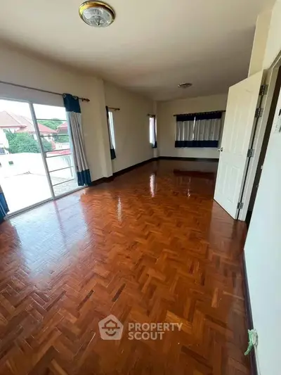 Spacious empty room with polished wooden floors and large windows offering natural light.